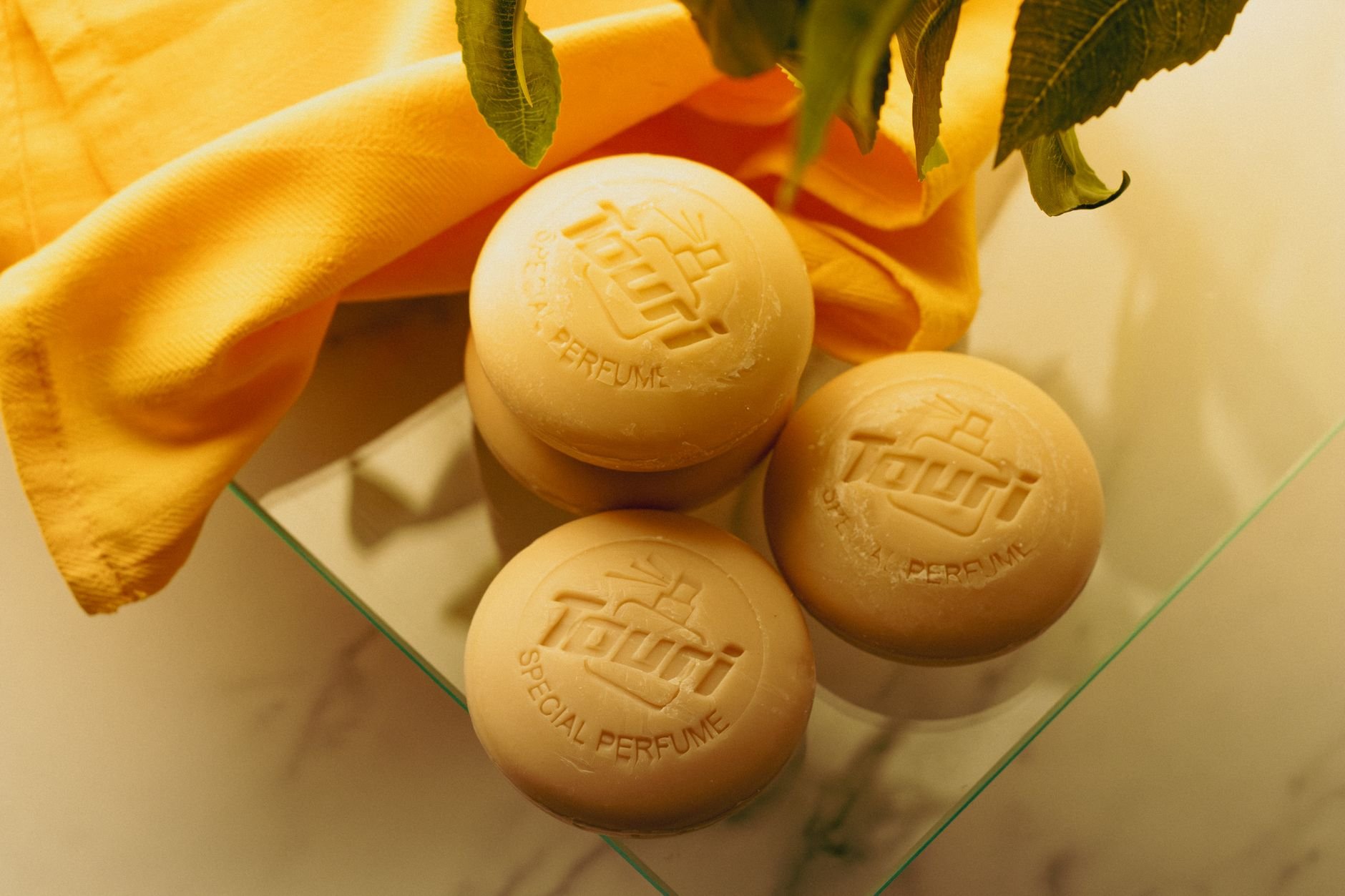 Elegant display of natural soap bars and a yellow towel on glass with a fresh aesthetic.