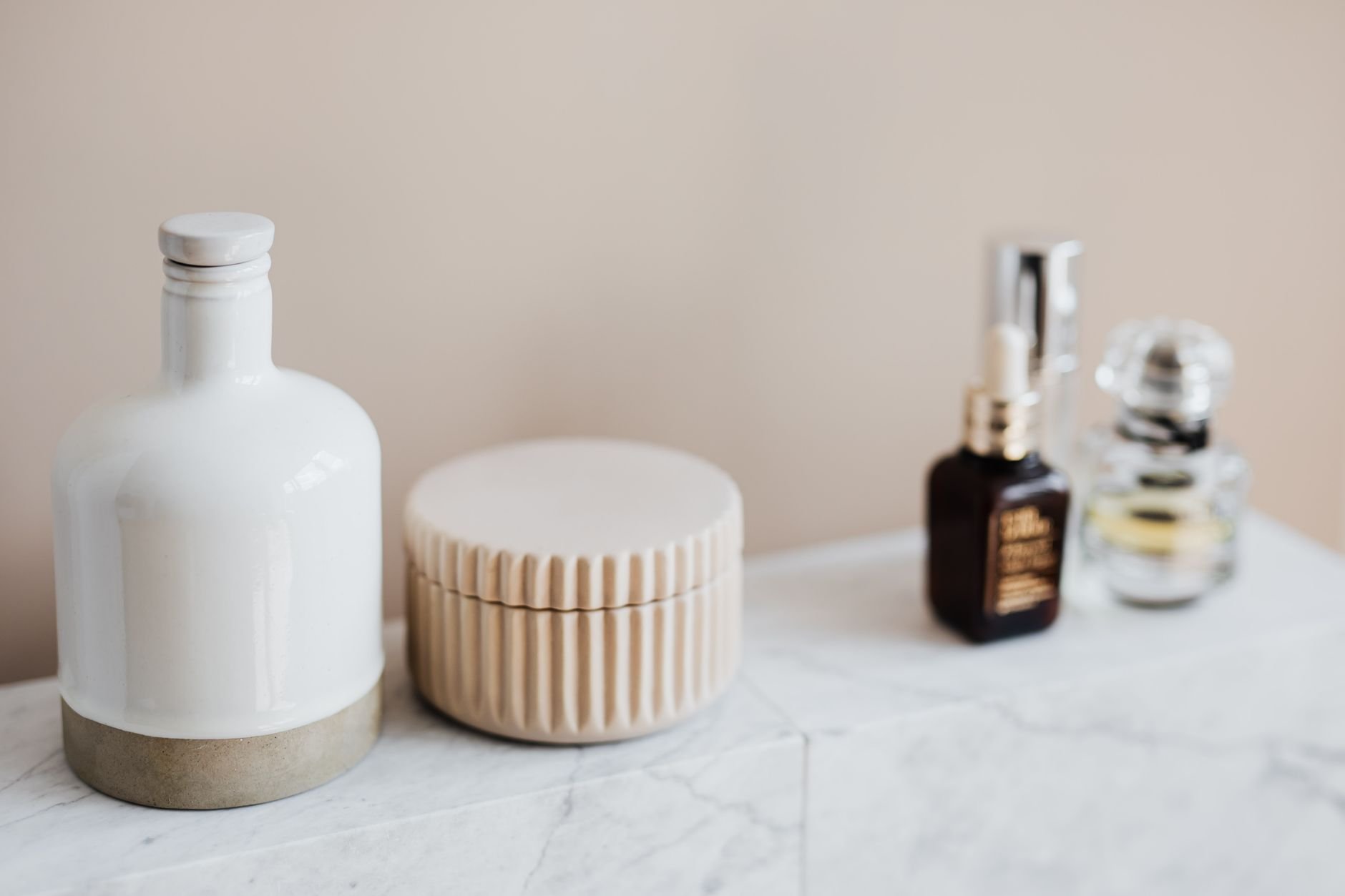 Natural cosmetics and perfume bottles arranged on a marble shelf against a warm beige wall.