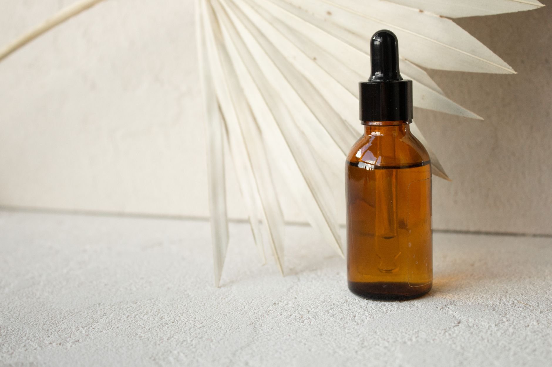 Amber glass dropper bottle beside a dried palm fan leaf on a textured surface.